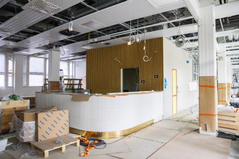 Valmiiksi rakennetun valkoisen infotiskin edessä on vielä rakennustarvikkeita ja takana on ohutta puunväristä pystyrimaa.