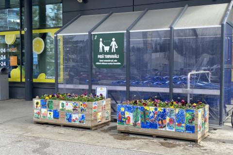 Violets planted in wooden boxes in the yard of the S-market in Kaukajärvi. The sides of the planting boxes are decorated with colorful drawings painted by children.