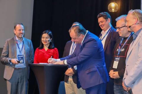 Ihmiset seisovat tapahtumalavalla katsomassa, kun Teppo Rantanen allekirjoittaa sopimusta. 