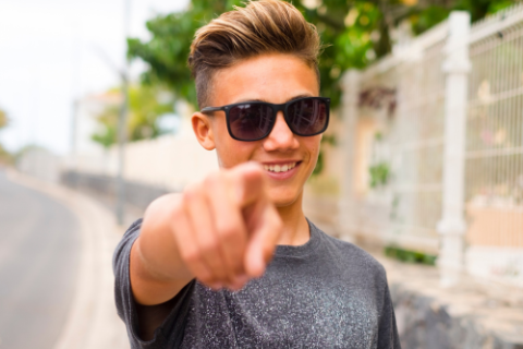 Young person is standin outside and pointing you with a smile.