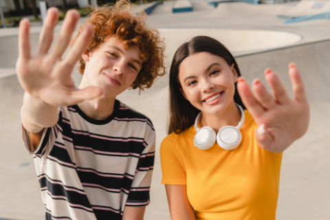 Two young people wave at the camera and smile.