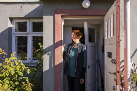 A person stands in the hallway of an old detached house with the doors open and looks out into the yard.