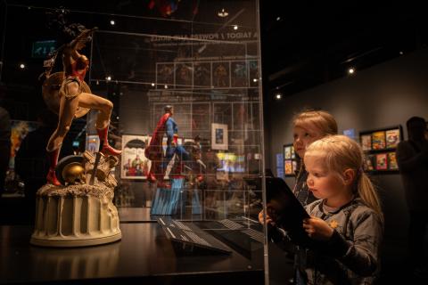Children look at superhero characters in a showcase.