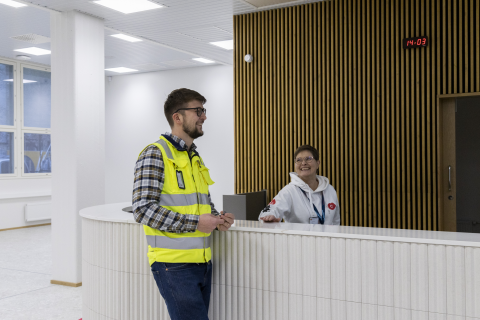 A tall white counter with one person standing in front of it and one behind it.