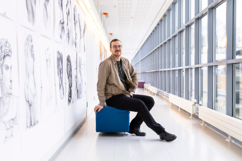 Apulaisrehtori Taimo Halme istuu jakkaralla koulun käytävällä, jonka seinällä on piirustuksia ja isoja ikkunoita.