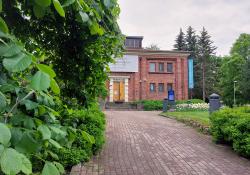 Tampereen taidemuseon tiilirakennus näkyy osittain vihreän kasvuston takaa.